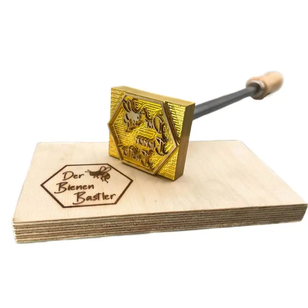 Anbei sieht man einen Stempel der sich ideal für Imker eignet. Als Rahmen dient eine Bienenwabe die den Text der Bienenbastler enthält. Unterteilt ist er hierbei in seine einzelne Wörter untereinander folgend aufgereiht. Rechts von der Schrift befindet sich eine stilisierte Biene. Die Platte selbst wird hierbei extern beheizt und liegt auf einer Holzplatte welche mit dem Motiv gebrandet wurde.