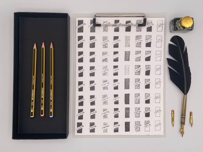 Ein Bild von einem Entstehungsprozesses eines Logos mit links daneben liegenden Bleistiften und rechts davon sind eine Tuschefeder mit und einem Tintenfäßchen.