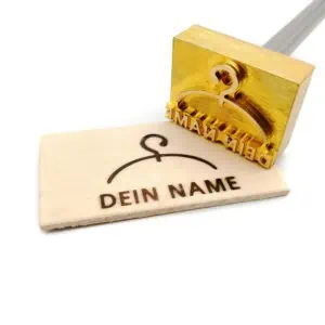 Dieser Stempel hat einen Kleiderbügel als Motiv und unterhalb davon befindet sich ein Schriftzug in großen Lettern mit „dein Name“. Der Schriftzug kann auf Kundenwünsche und in unterschiedlichen Ausführungen angepasst werden. Zu sehen ist der Stempel hierbei in der externen Ausführung als Probedruck auf einer kleinen Holzscheibe. Anbei ist das Motiv in elektrischer Ausführung fotografiert. Ein Brennkolben mit schwarzem Griff und einem Edelstahlkolben gefolgt von der Messingstück. Das Gerät liegt auf einem aufgeklappten Ständer. Ein gefräst ist das Motiv in einer Messingplatte und wurde auf ein kleines Stück Holz eingebrannt.