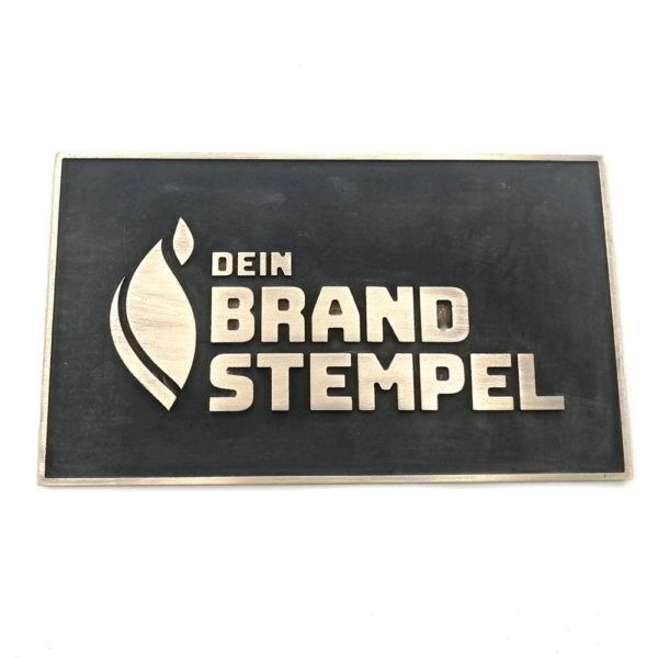 Hier ist ein Messingschild zu sehen, welches schwarz patiniert wurde. Die Schrift sticht dabei golden hervor und wird von einem Steg umrahmt. Als Motiv wurde das Logo der Firma Brandstempel verwendet.