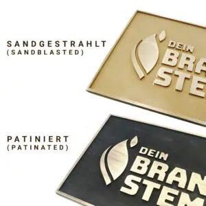 Zwei Hälften von Messingschildern sind zu sehen eines davon patiniert, die andere ist sandgestrahlt.