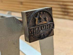 In der Nahaufnahme ist eine verschmutzte Brennplatte zu sehen, die an einem Eisenstab verschraubt ist und auf einer Ablage ruht.