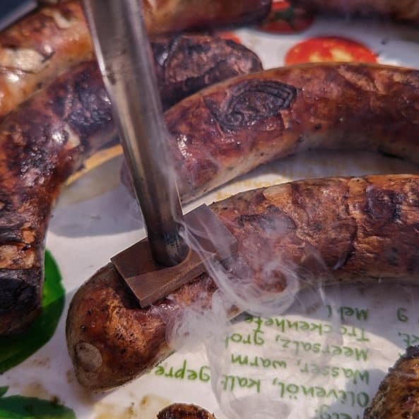 Das Bild zeigt eine Bratwurst, die per Grillstempel signiert wird.