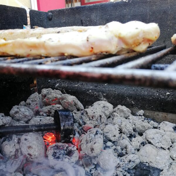 Das Foto zeigt einen Grill mit Grillgut und Grillbrandeisen.