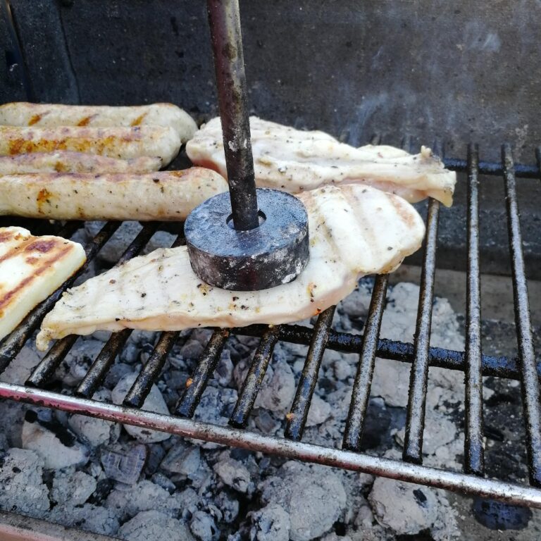 Das Bild zeigt ein Steak, das auf dem Grillrost mit einem Grillstempel bearbeitet wird.