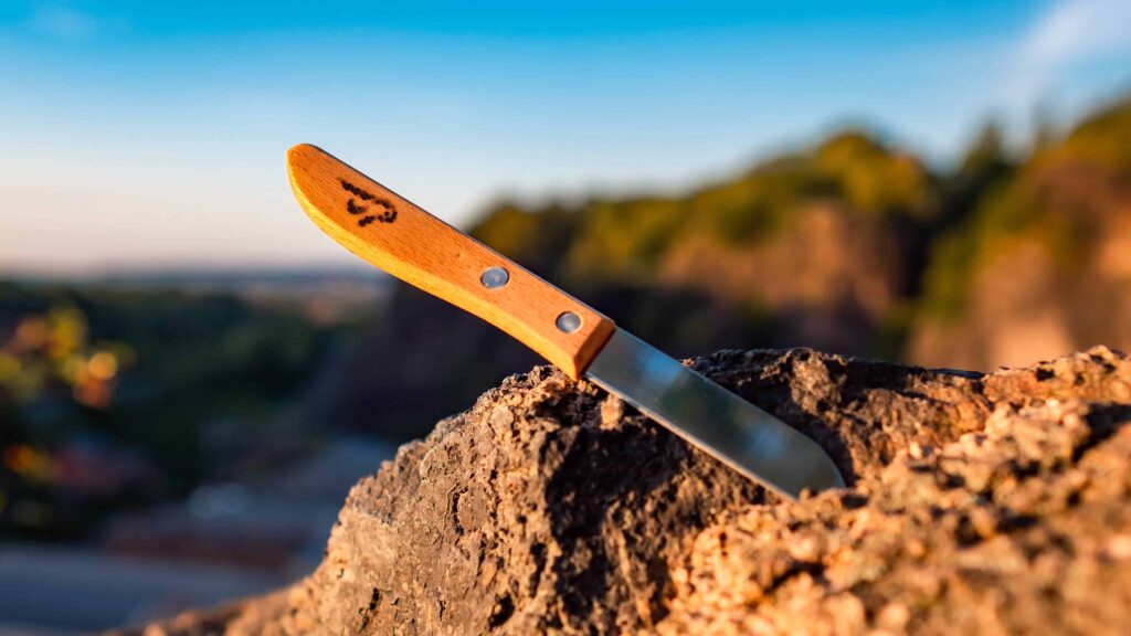 Das Bild zeigt ein Messer mit Handgriff aus Holz, das auf einem Steinhügel liegt.