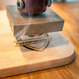 Das Foto zeigt einen elektrischen Heißprägestempel, der auf ein Holzschneidebrett brandet.