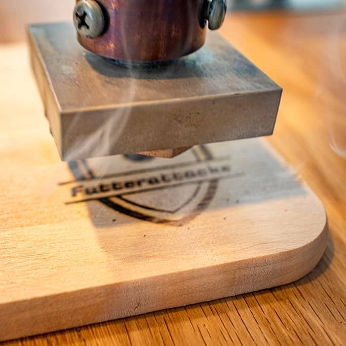 Das Foto zeigt einen elektrischen Heißprägestempel, der auf ein Holzschneidebrett brandet.