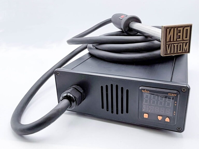 Das Bild zeigt eine schwraze Box, an dem ein Kabel angeschlossen ist. Am Ende des Kabels befindet sich ein Handgriff mit einem Brennstempel.